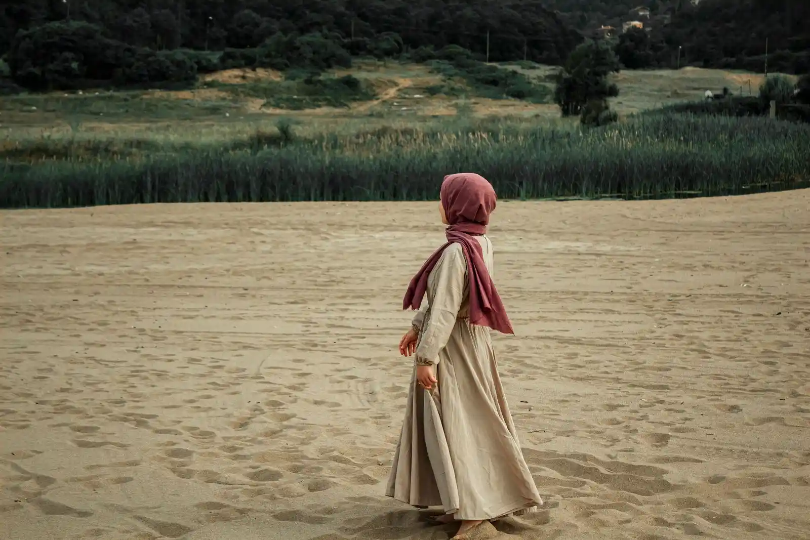 A woman in a hijab walking on a sandy shore